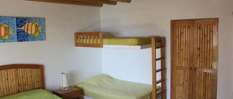 Habitación con literas, techo de madera, una cama individual con colcha verde, una mesita de noche, un cuadro de peces en la pared y un armario de madera.