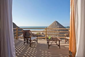 A wooden deck with wicker furniture and a thatched roof structure, overlooking a beach and ocean. - Soleil Bungalows (Los Organos)