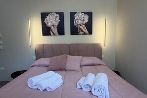 A hotel room with a bed, pillows, and towels. There are two wall-mounted light fixtures and two paintings above the bed.