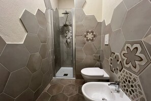 Ein Badezimmer mit sechseckigen Fliesen, einer Glasdusche, einer Toilette und einem Waschbecken.