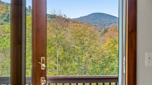 A view from a balcony with a wooden railing, overlooking a forested area with autumn foliage and a hill in the distance. - The Getaway: Relax with hot tub, fire pit, and mountain views—just 15 mins from Killington slopes! (Pittsfield)