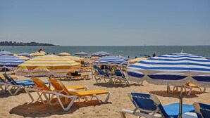 A beach with rows of sun loungers and striped beach umbrellas.