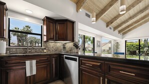 Una cocina moderna con alacenas de madera oscura, salpicadero de piedra y un amplio ventanal con vista a palmeras.