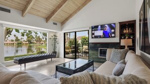 Una sala de estar moderna con un televisor grande, asientos cómodos, una chimenea y vistas a un lago y vegetación.