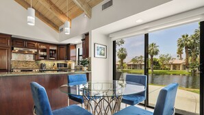 Cocina moderna con una mesa de comedor de vidrio y sillas azules, con vista a un cuerpo de agua y palmeras.