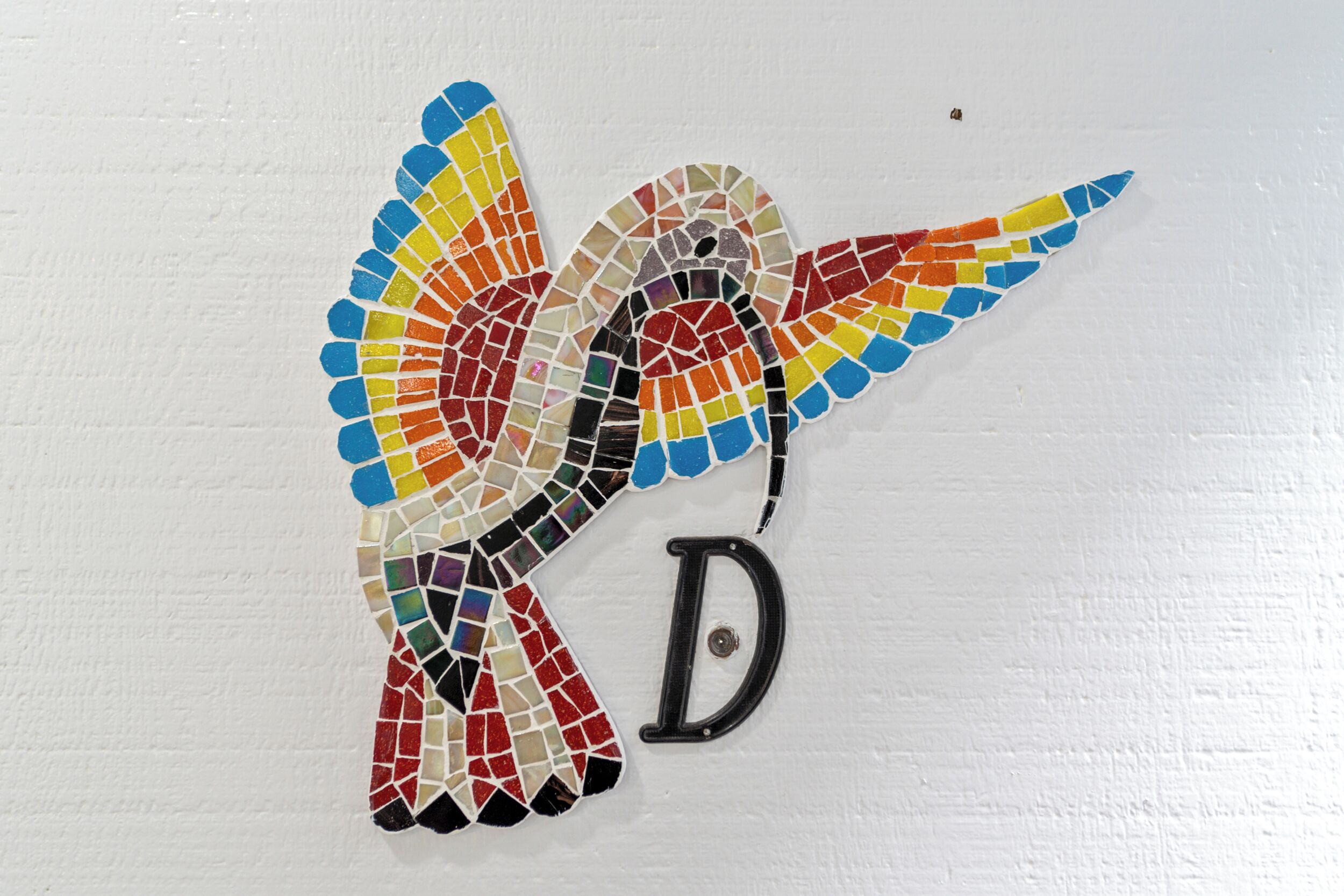 Une mosaïque représentant un colibri, avec la lettre « D » en dessous.