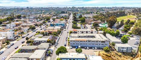 A residential area with a mix of single-family homes and small apartment buildings, featuring a central street with parked cars and a clear sky.