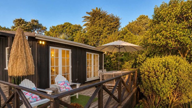 Une terrasse en bois avec des sièges d’extérieur, un parasol en chaume et une vue sur un jardin luxuriant.