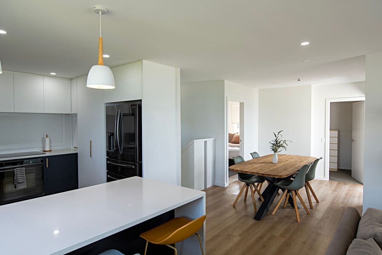 Une cuisine moderne avec des meubles blancs, un îlot central et un coin repas comprenant une table et des chaises en bois.