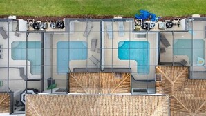 Vista cenital de un área de piscina con varias piscinas, zonas de descanso y una sección cubierta con servicios junto a la piscina.