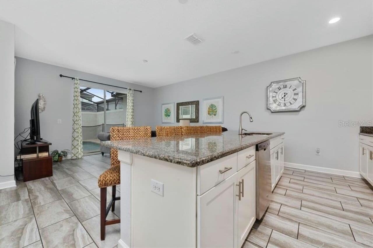 A modern kitchen with white cabinets, a granite countertop, and a built-in sink. There is a clock on the wall and framed pictures above the counter.