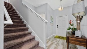 Una escalera con peldaños alfombrados, una puerta blanca, una lámpara fijada a la pared y una pequeña mesa con una planta.