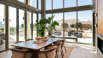 A modern dining area with a large table and chairs, large windows, and a view of the outdoors.