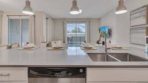 A modern kitchen with a large island, stainless steel appliances, pendant lighting, and a view of the outdoors. - Go 31- Champions Gate (Kissimmee)