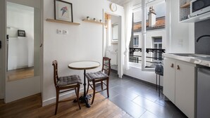 Una cocina moderna con armarios blancos, una mesa de comedor de madera y dos sillas. Hay una ventana que ofrece vistas a un edificio con tejado de baldosas.