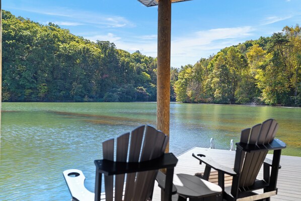 A deck with Adirondack chairs overlooking a lake with a forested shoreline.