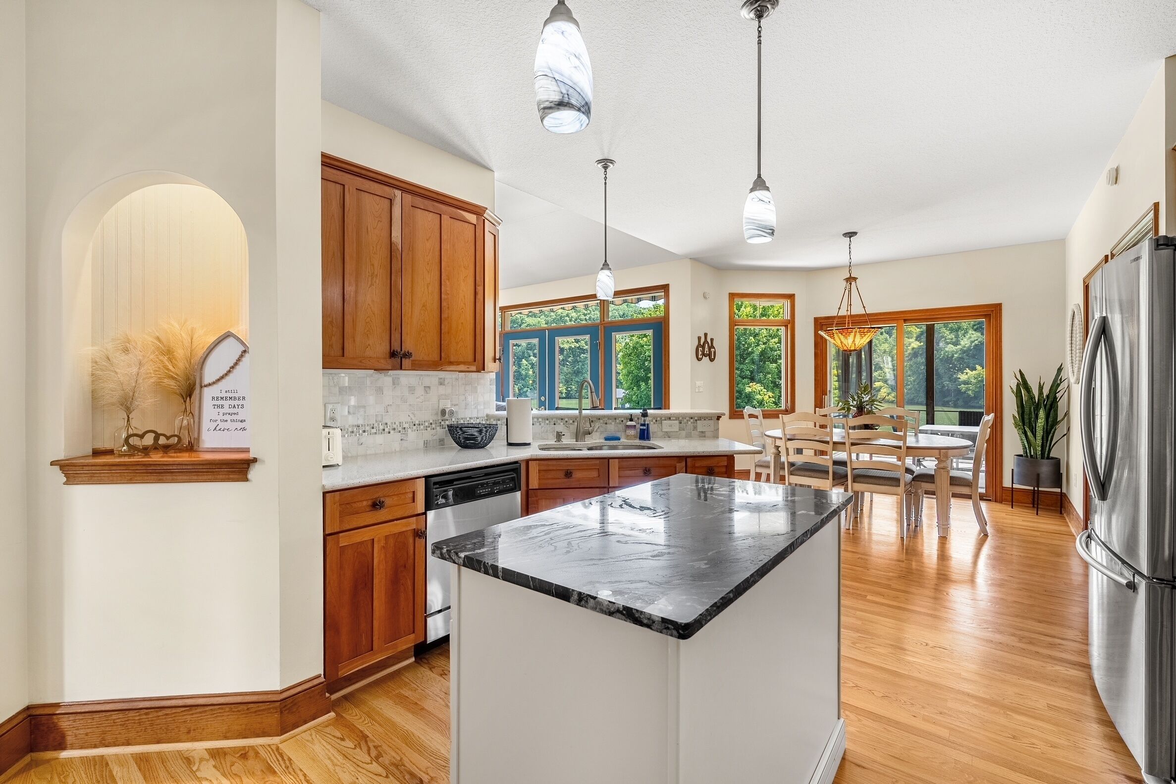 A modern kitchen with wooden cabinets, a marble countertop island, and pendant lighting.