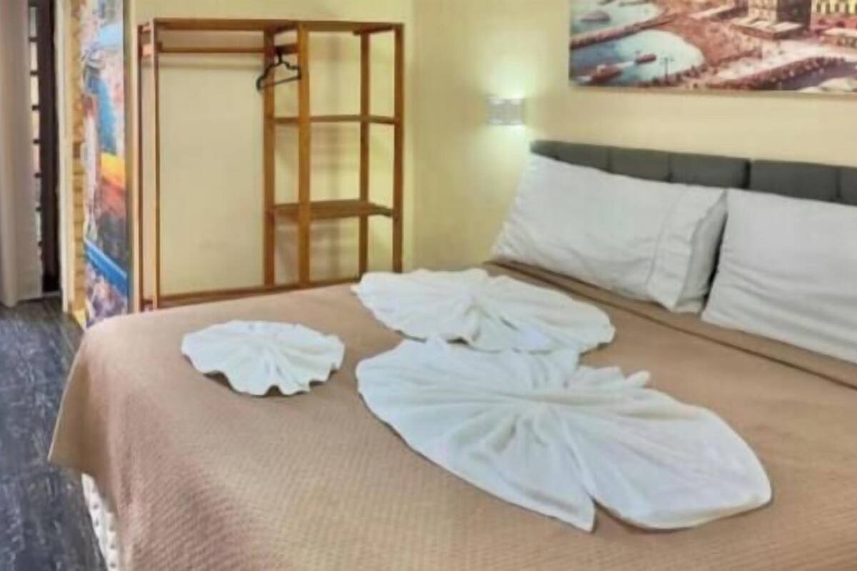 A hotel room with a bed, a wooden wardrobe, a painting on the wall, and a view of the outside.