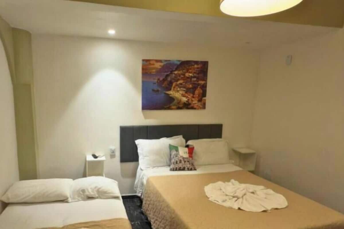 A hotel room with a bed, a nightstand, a TV mounted on the wall, and a painting above the bed.
