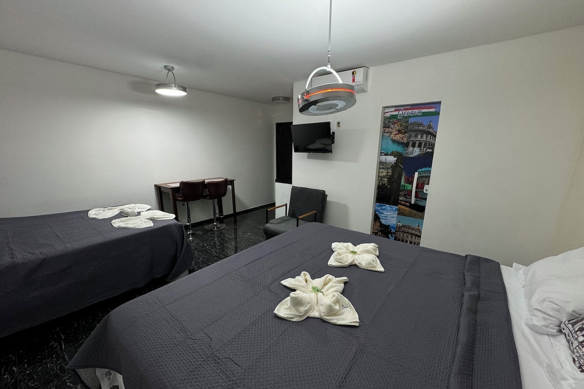 A hotel room with two beds, a desk, two chairs, a TV, and a poster on the wall.