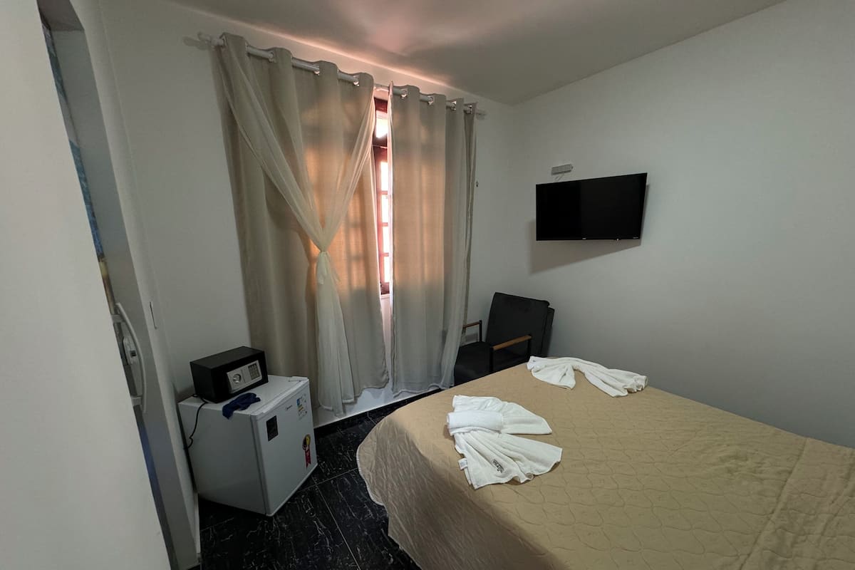 A hotel room with a bed, a TV mounted on the wall, a desk with a microwave, and a chair.