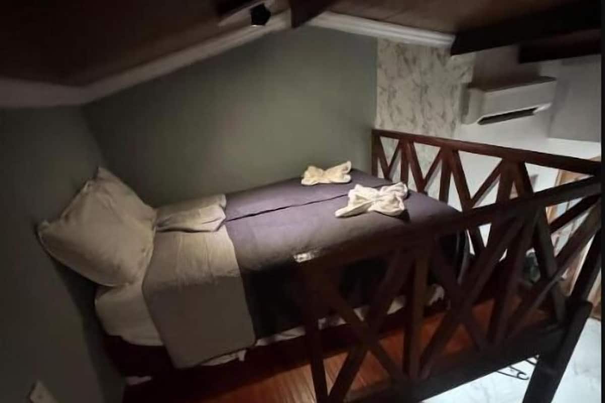 A room with a bed, a wooden chair, and a staircase.