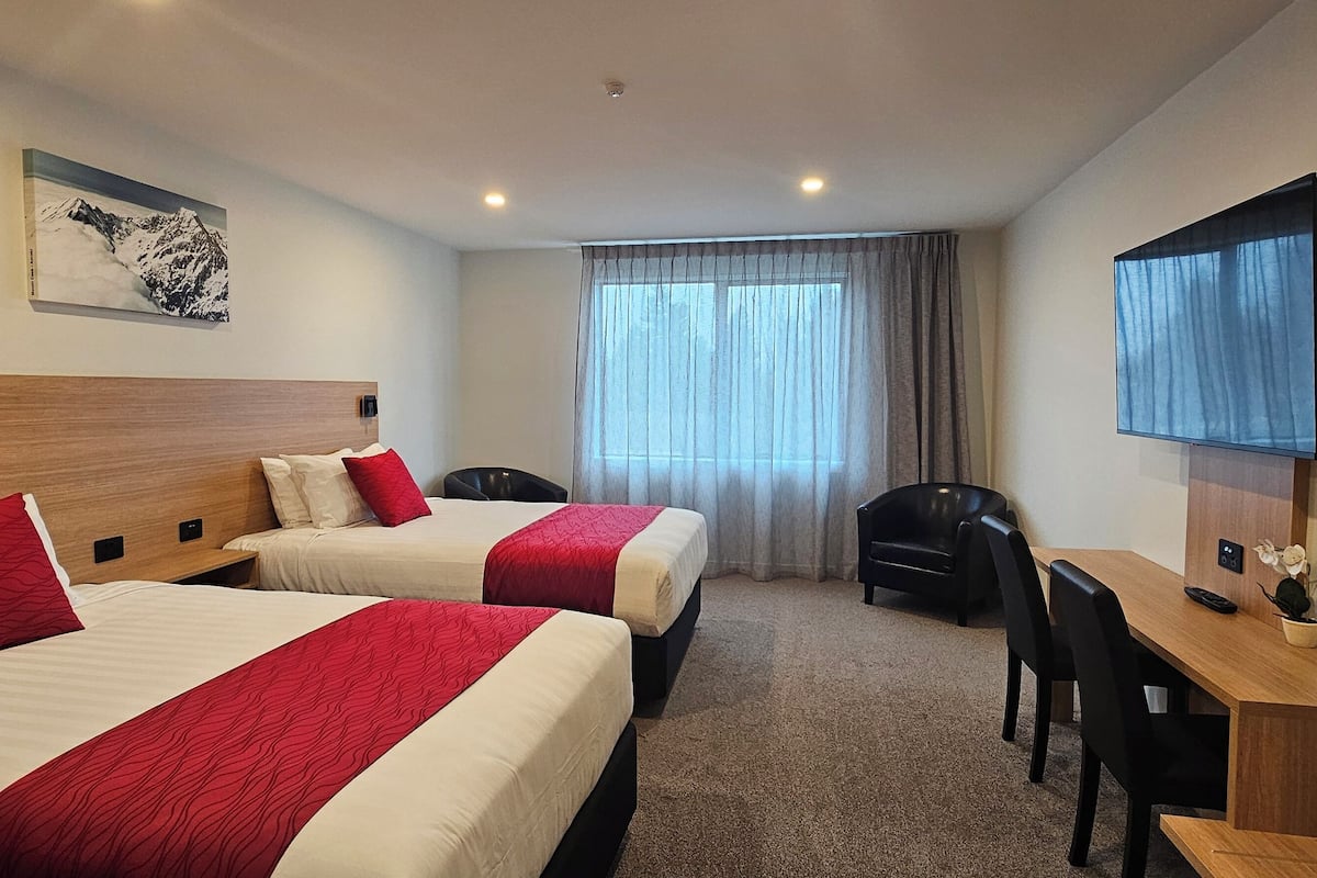 A hotel room with two beds, a desk, a chair, a TV, and a window with curtains.