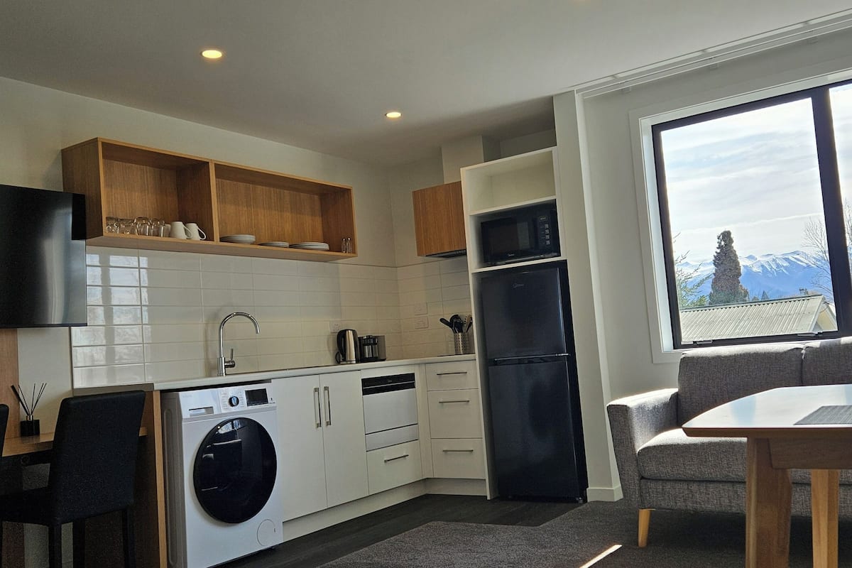 A modern kitchen with a washing machine, a dining area with a table and chairs, and a large window with a mountain view.
