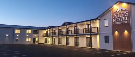 A two-story motel with a sign reading "ALPS MOTEL APARTMENTS" and a parking lot in front.