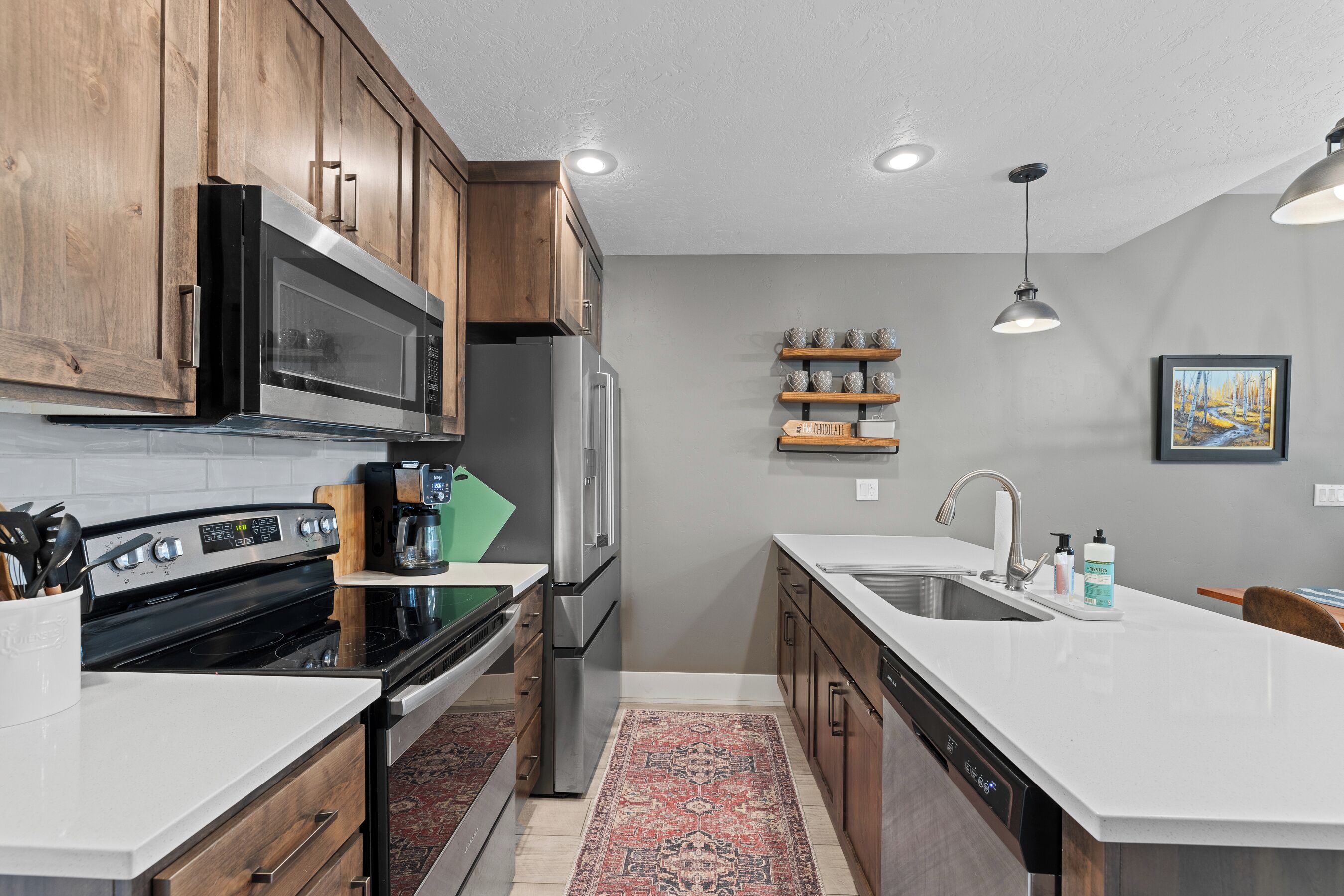 Una cocina moderna con armarios de madera, electrodomésticos de acero inoxidable, encimera blanca y alfombra roja estampada.