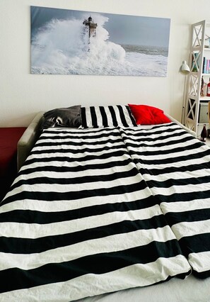 A bed with a striped blanket, pillows, and a painting of a lighthouse on the wall.