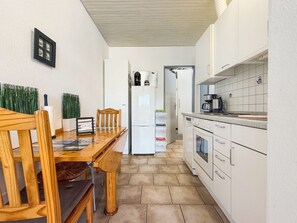 A compact kitchen with white cabinets, a wooden dining table, and a built-in oven.