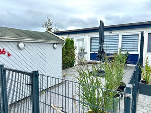 A caravan with a white exterior and a blue roof, a fenced outdoor area with plants, and a grey metal gate.