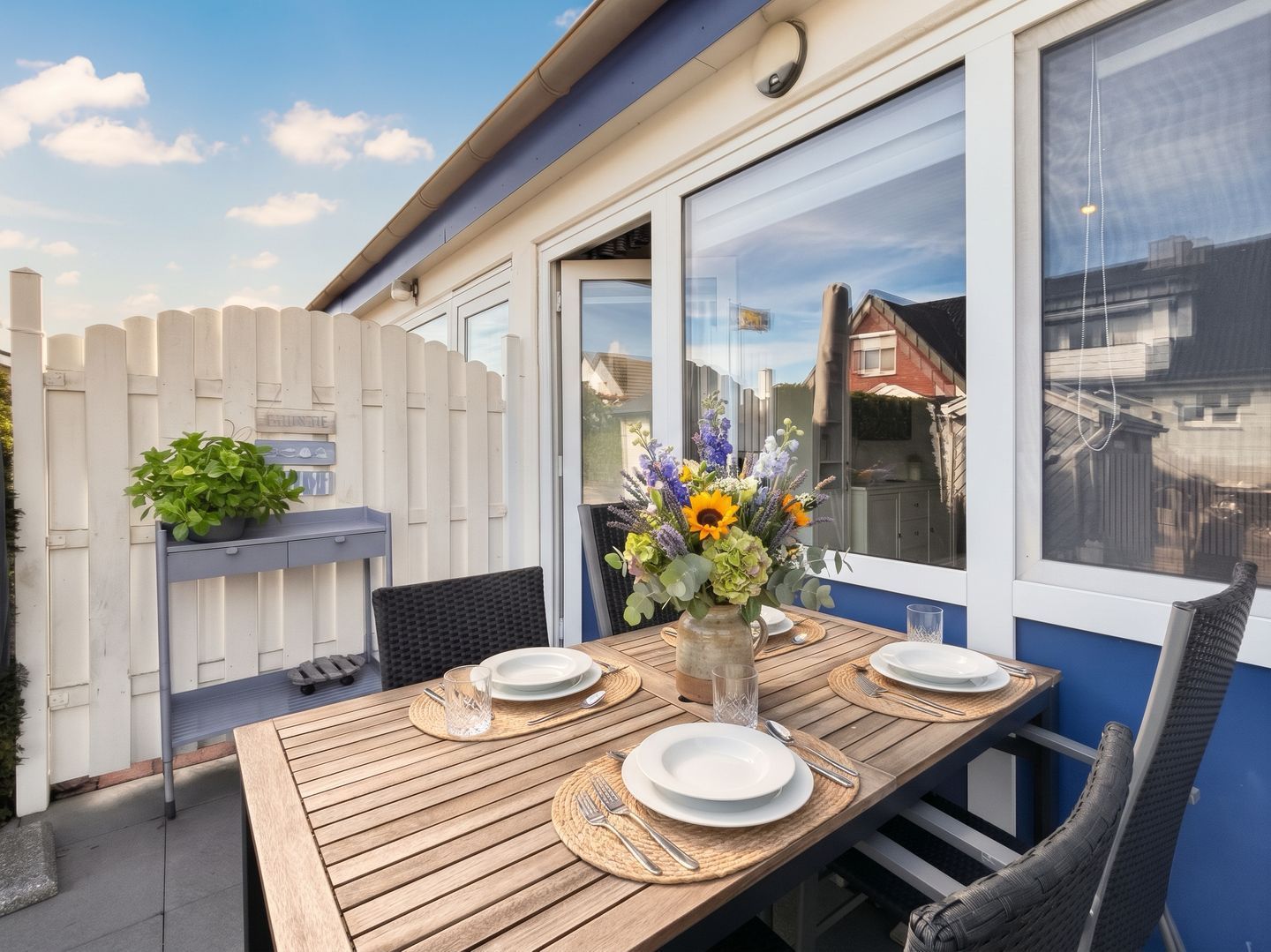 Un espace extérieur aménagé pour les repas, avec une table en bois, des chaises et un vase rempli de fleurs.