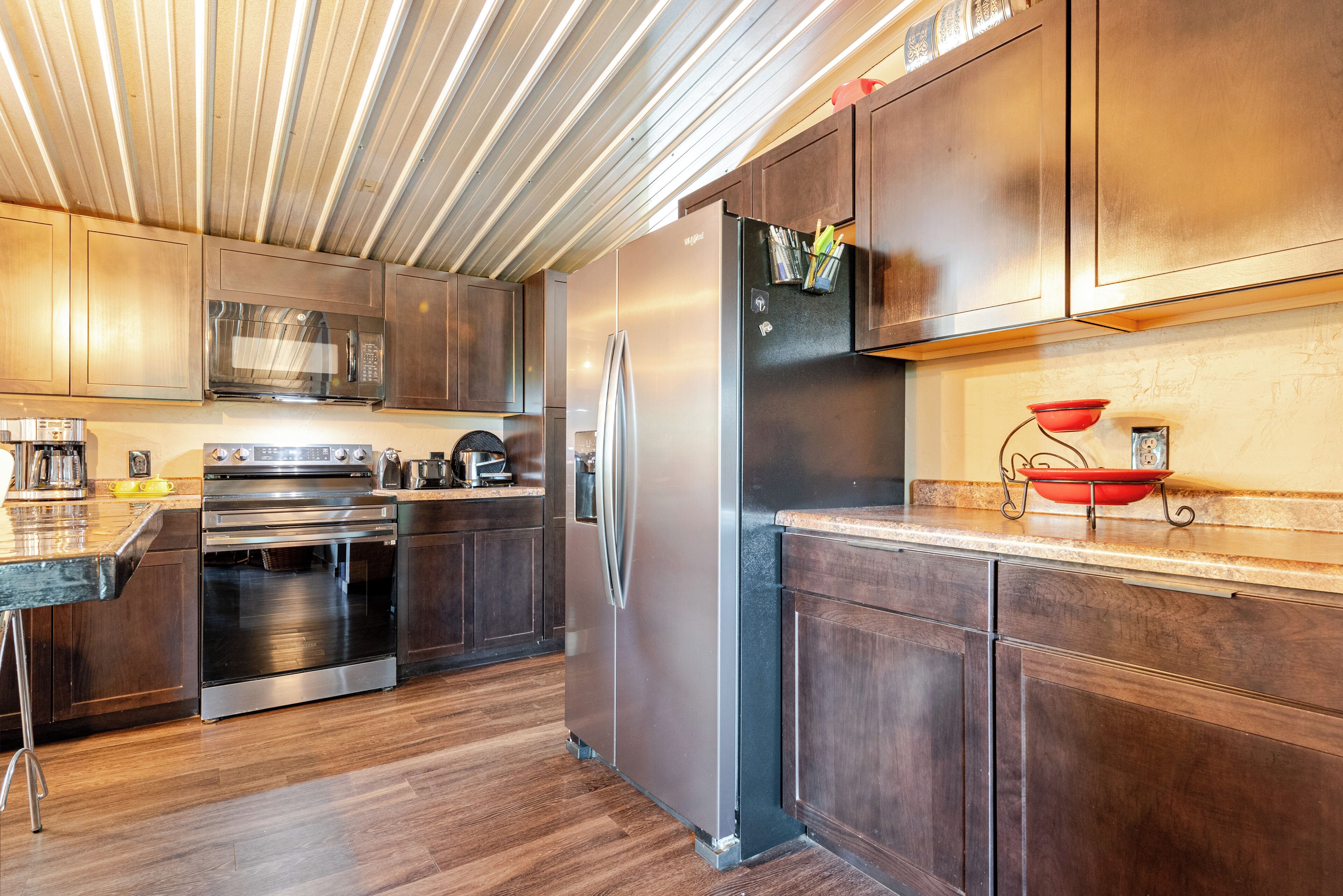 A modern kitchen with stainless steel appliances, wooden cabinets, and a wooden ceiling.