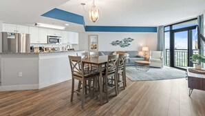 A modern kitchen with stainless steel appliances, a dining area with wooden chairs, and a living room with a sofa and a large window. - Caribbean 2002 (Myrtle Beach)