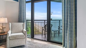 A room with a chair, a table with a lamp, and a view through a large glass door to an outdoor balcony with chairs. - Caribbean 2002 (Myrtle Beach)