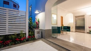 A modern hotel lobby with a tiled floor, a green sofa, a glass partition, and a statue of a flamingo.