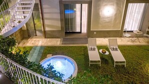 A modern outdoor area with a hot tub, lounge chairs, and a staircase leading to an upper level.
