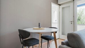 A small, modern room with a round table and two chairs, a door leading outside, and a grey sofa. - Blueground | Breite, elev, washer, balcony (Basel)