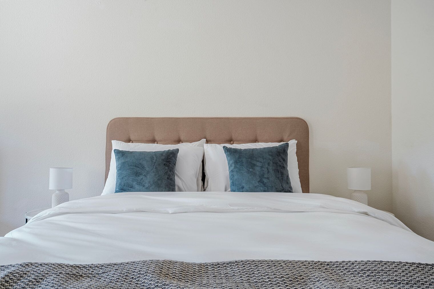 A neatly made bed with a headboard, two pillows, and two bedside lamps.