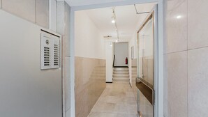 A hallway with a fire alarm panel, a fire extinguisher, and a staircase leading to another floor. - Blueground | Breite, elev, washer, balcony (Basel)