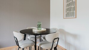 Ein runder Esstisch mit einer grünen Glasdekoration in der Mitte, umgeben von vier gepolsterten Stühlen mit schwarzen Metallgestellen.