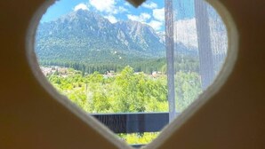 A heart-shaped window with a view of a mountain range and a town below. - Alpine River Home: Peace and Mountain View (Bușteni)