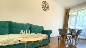 A teal sofa, a round coffee table, and a dining area with chairs and a table. - Alpine River Home: Peace and Mountain View (Bușteni)