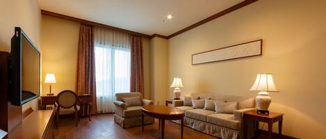 Habitación de hotel con piso de madera, un conjunto de sofás, un televisor y una obra de arte enmarcada en la pared.
