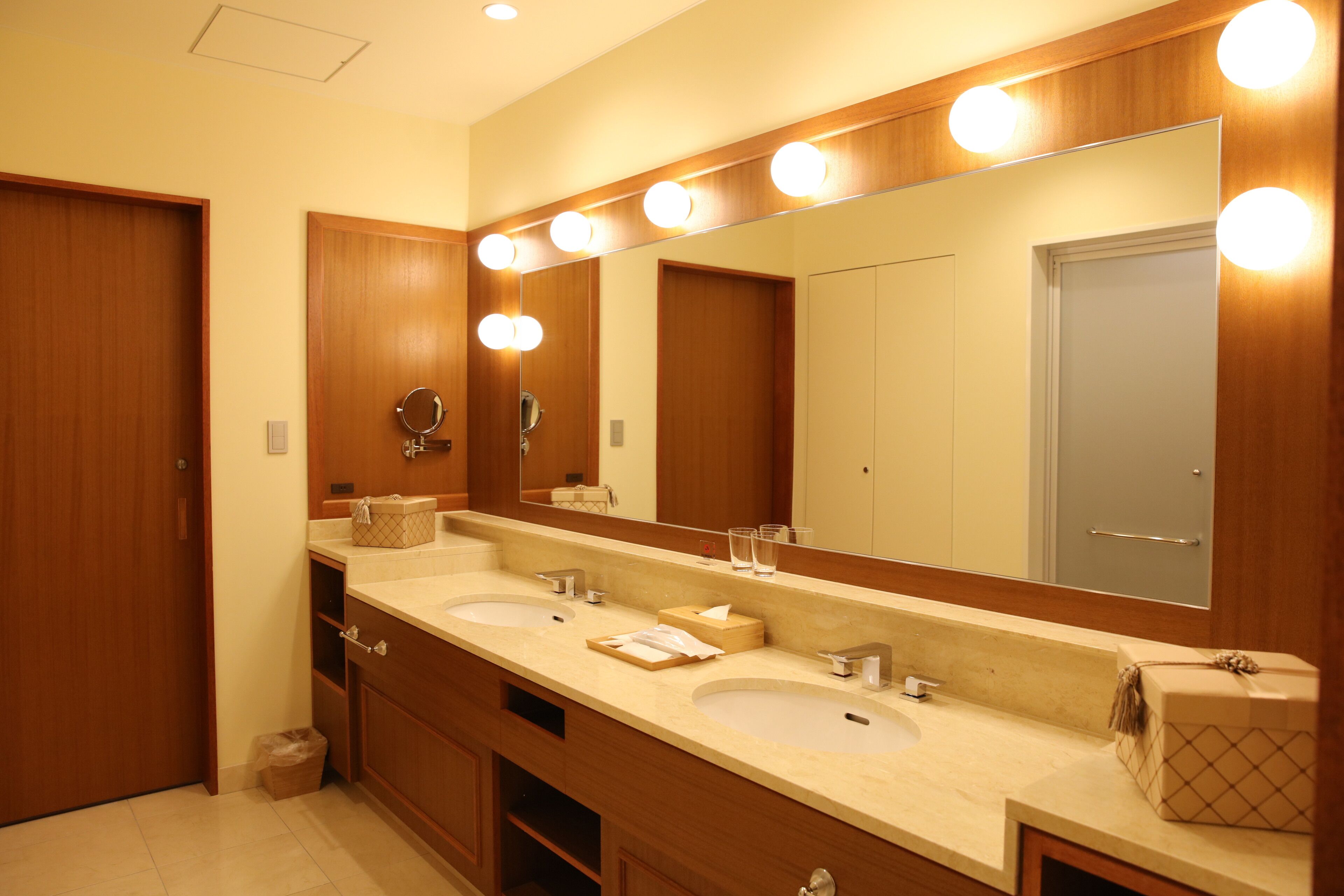 A hotel bathroom with two sinks, a large mirror, and overhead lights.