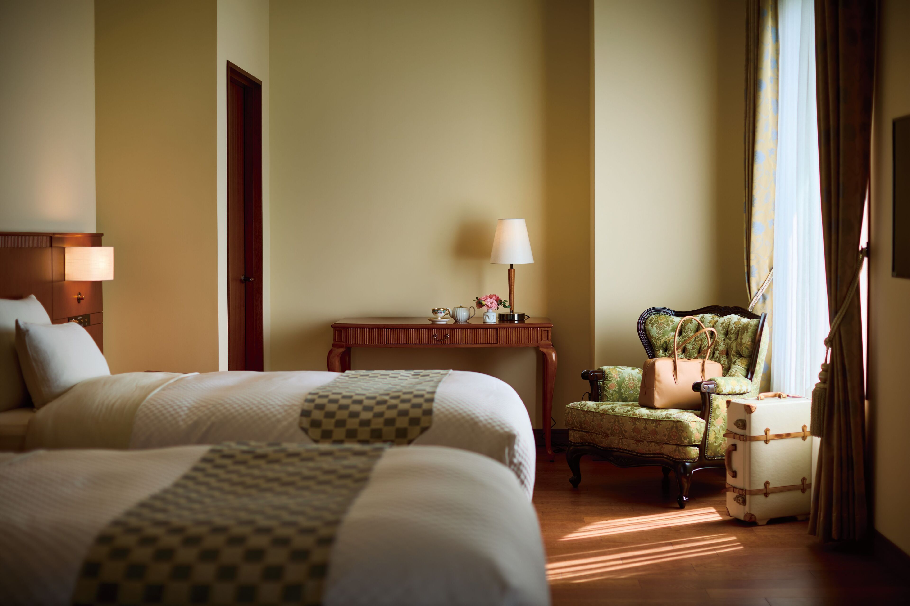 A hotel room with a large bed, a desk with a lamp, a chair, and a suitcase.