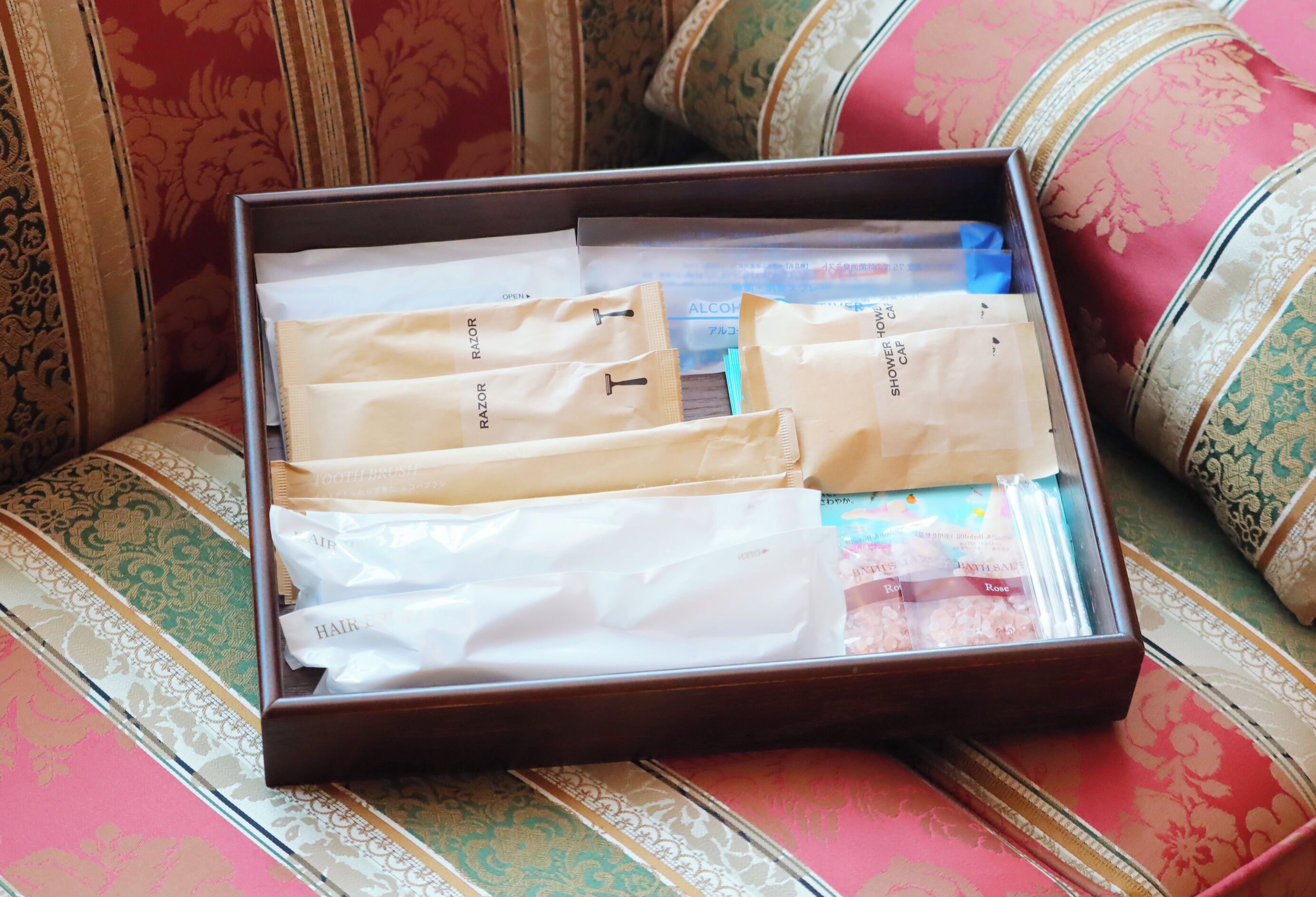 A wooden box with various toiletries on a patterned sofa.