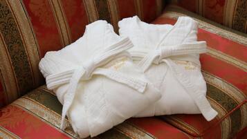 Duas camisas brancas com a inscrição 'Grand Emporio Hotel' bordada, colocadas em um sofá com padrão em vermelho e dourado.